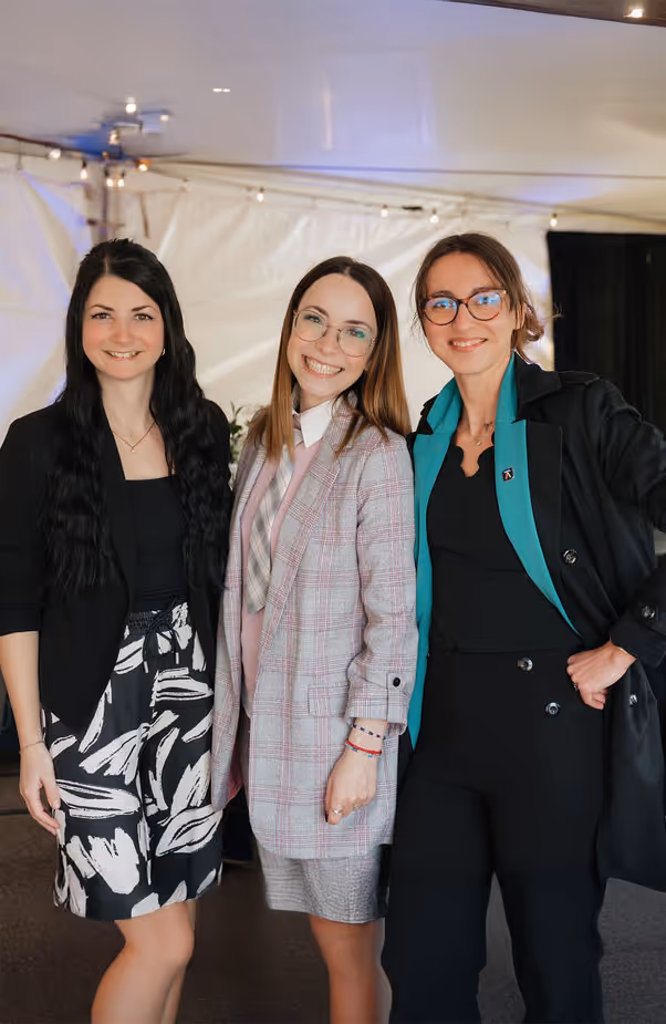 Trois femmes souriantes posant ensemble dans un espace intérieur éclairé sous une tente.