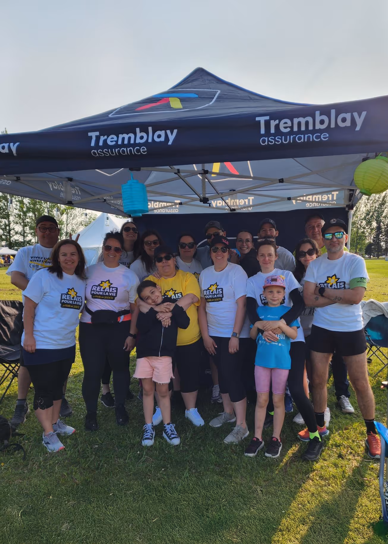 Groupe de personnes de tous âges posant sous un chapiteau Tremblay assurance lors d'un événement en plein air.