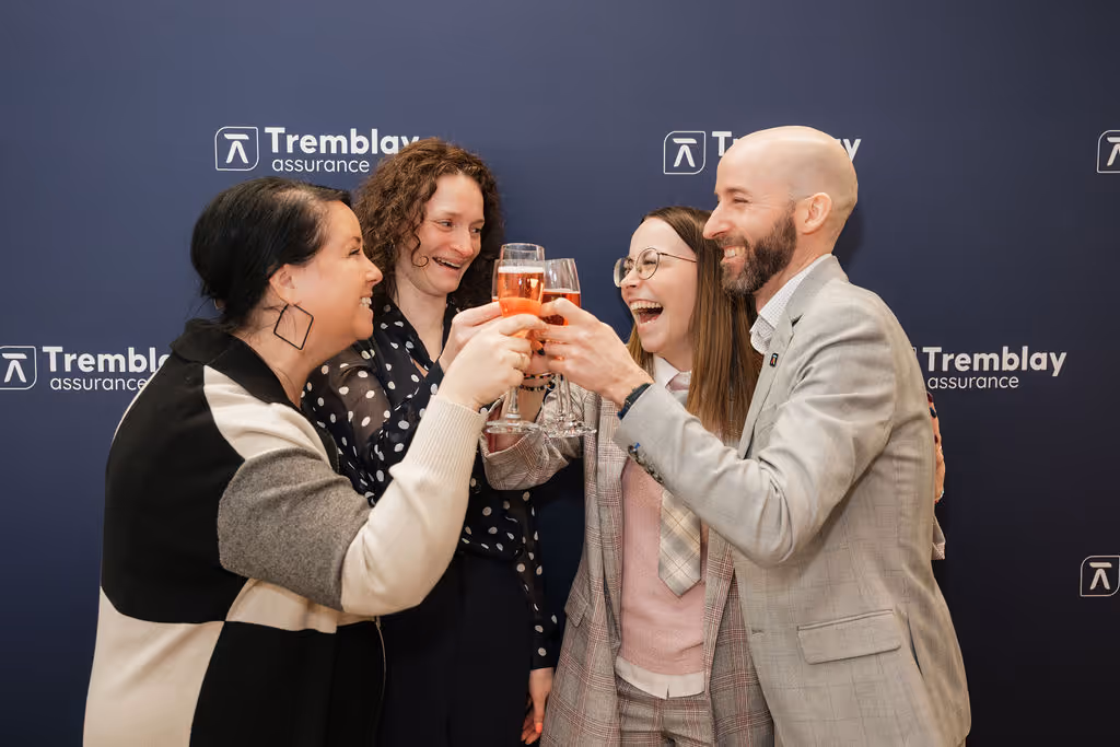 Quatre personnes souriantes trinquent avec des verres de vin devant un mur bleu avec le logo Tremblay assurance.