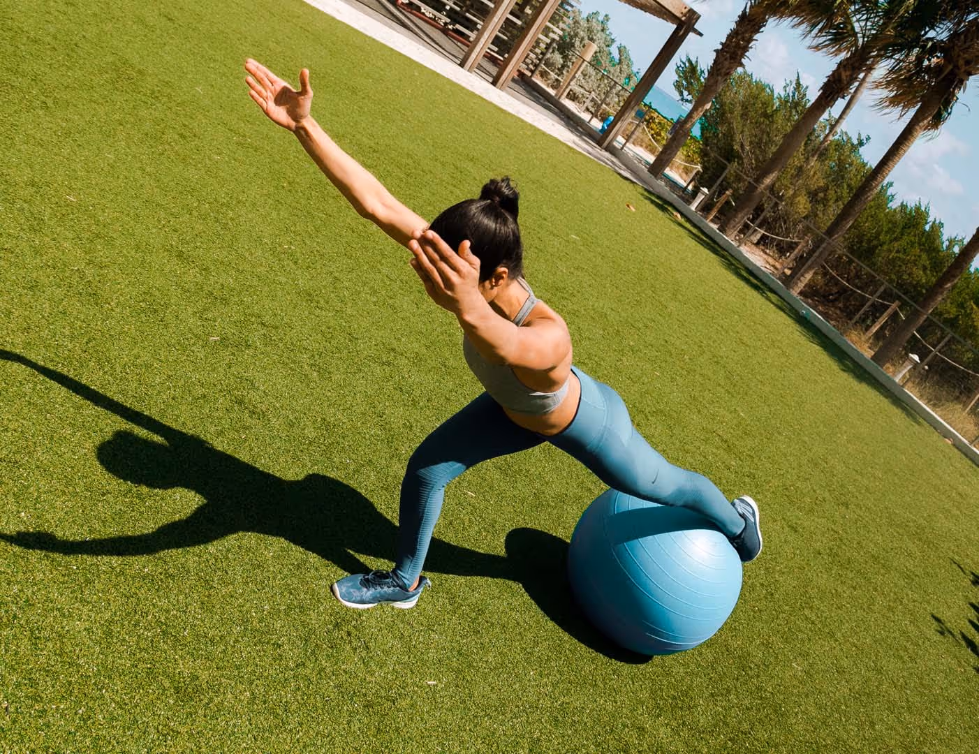 Woman performing a stability core exercise using a Pilates ball outdoors.