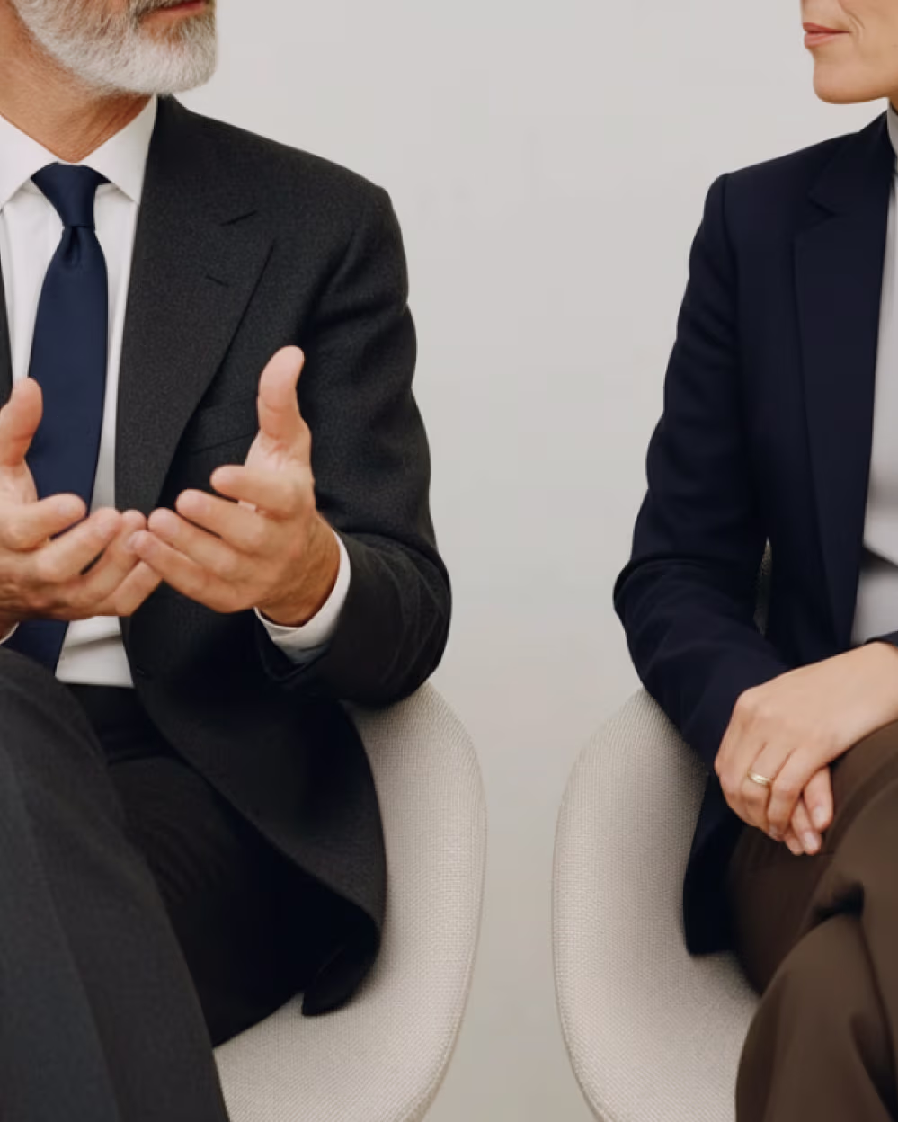 Two professionally dressed people seated and engaged in conversation, focusing on their hands and torsos.