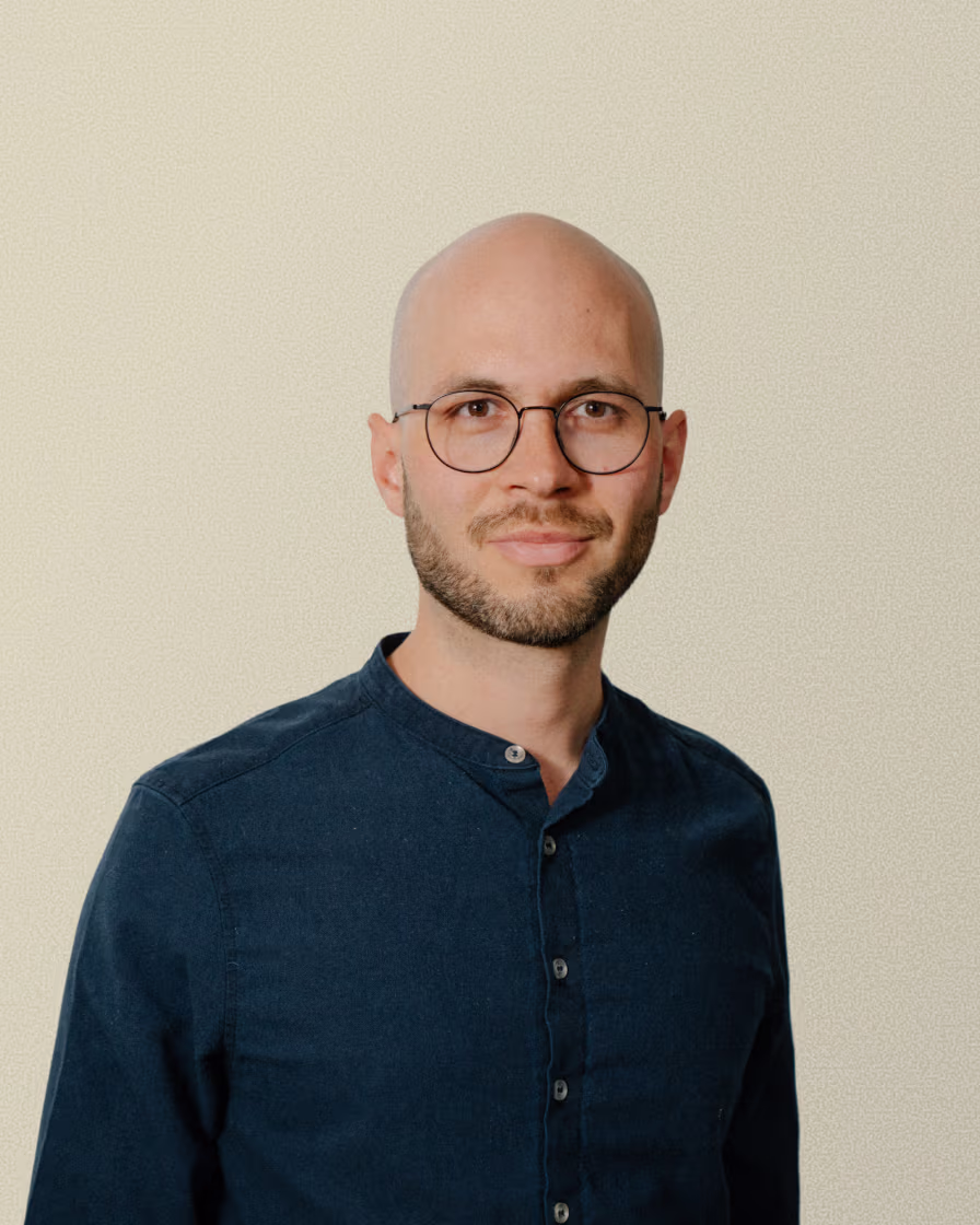 Portrait of a bald man with glasses and beard wearing a dark blue button-up shirt.