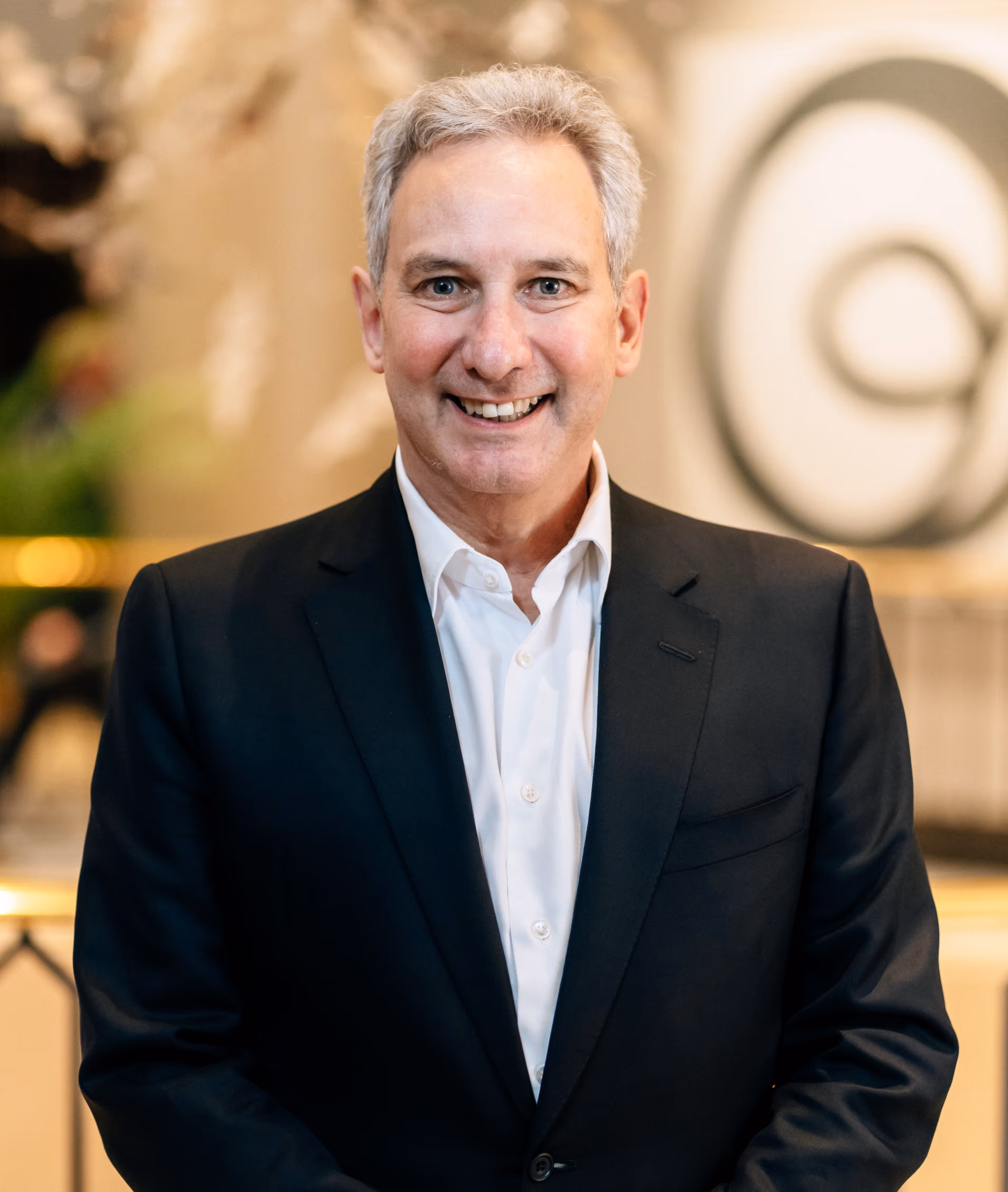 Smiling middle-aged man with gray hair wearing a black suit jacket and white shirt.