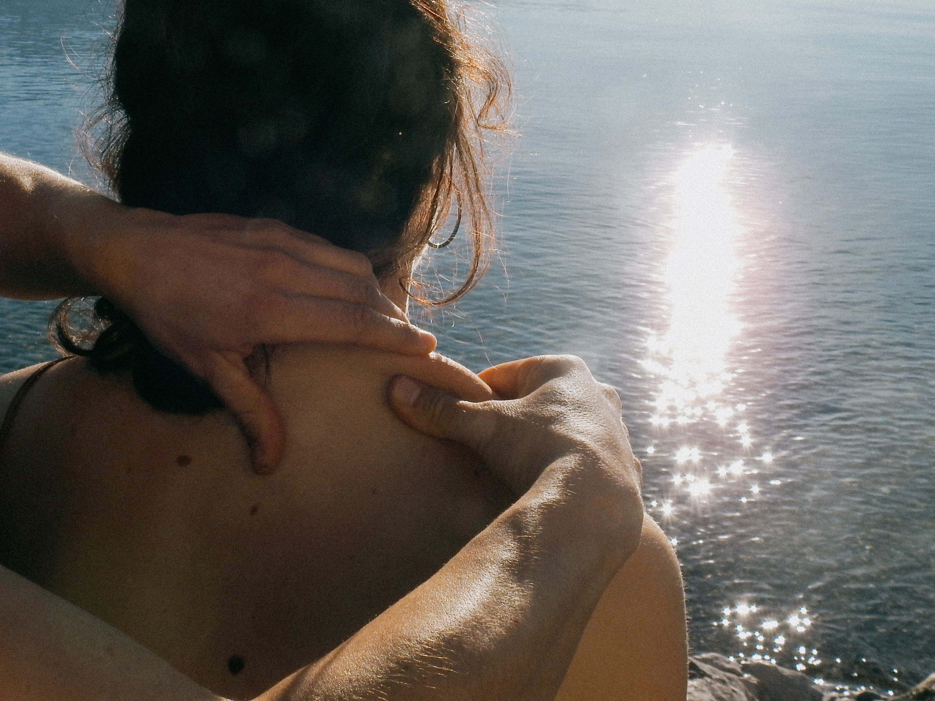 Close-up of hands giving a shoulder massage against a backdrop of shimmering water.