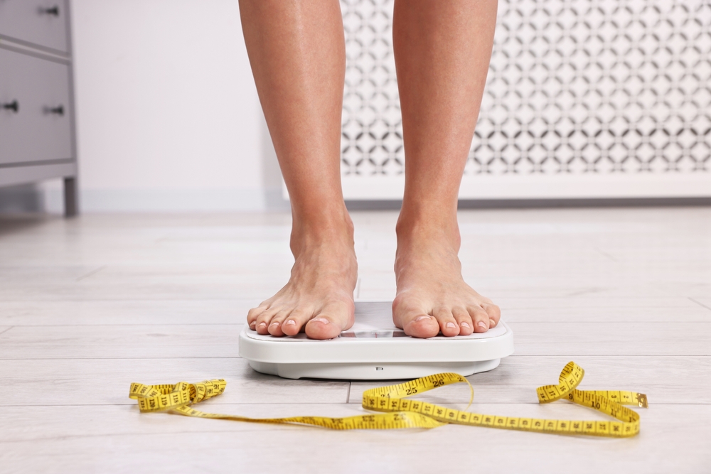 feet of a woman weighting herself and measuring her waist.