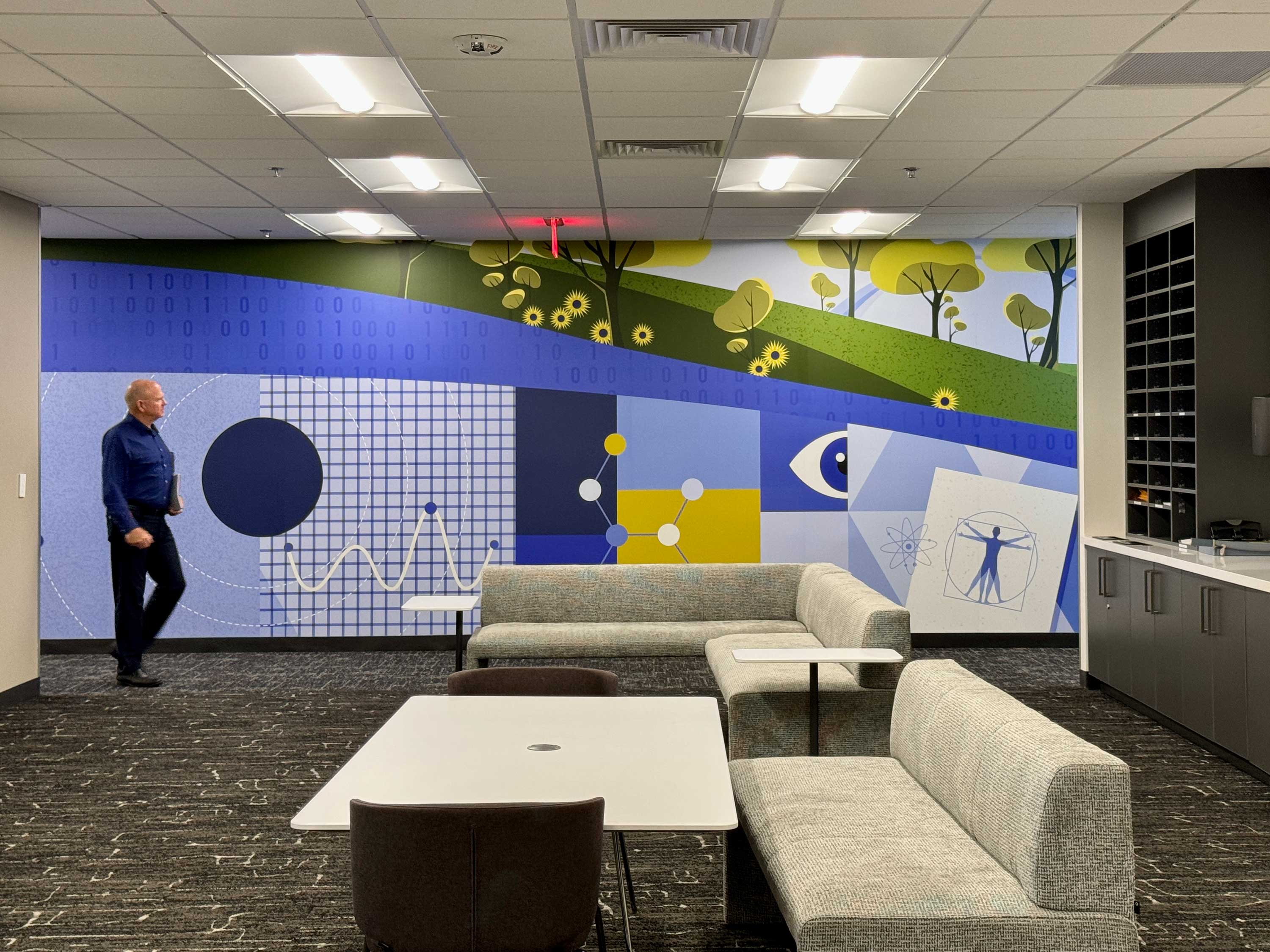 Modern office lounge area with sectional sofas, white tables, and a large colorful mural featuring scientific and nature-themed graphics on the wall.Experiential graphics installation at American Express Desert Ridge Campus, Phoenix, Arizona