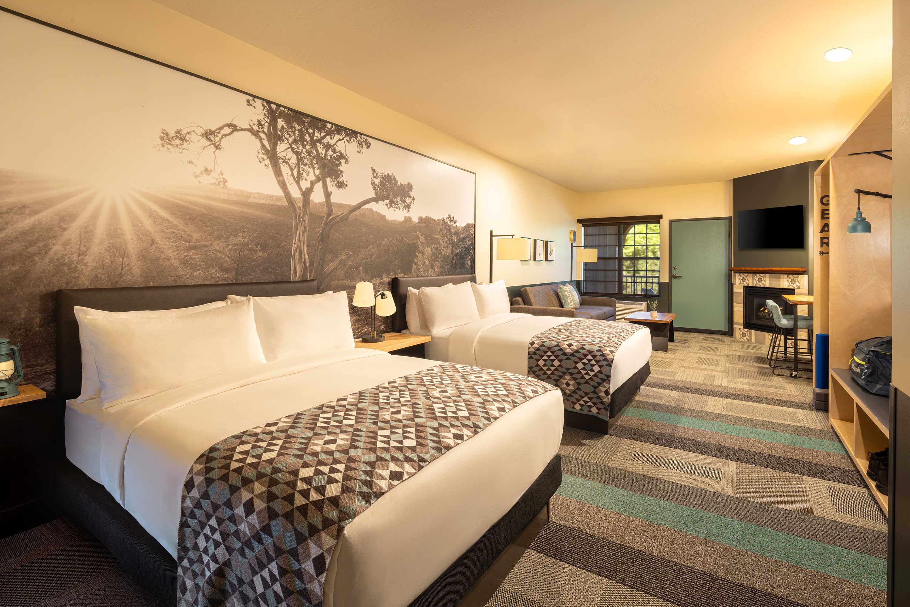 Cozy hotel room with a king-sized bed, starry night mural, patterned blanket, large window with forest view, and fireplace. Mountain Modern Motel Sedona, experiential design by Liz Taylor Creative