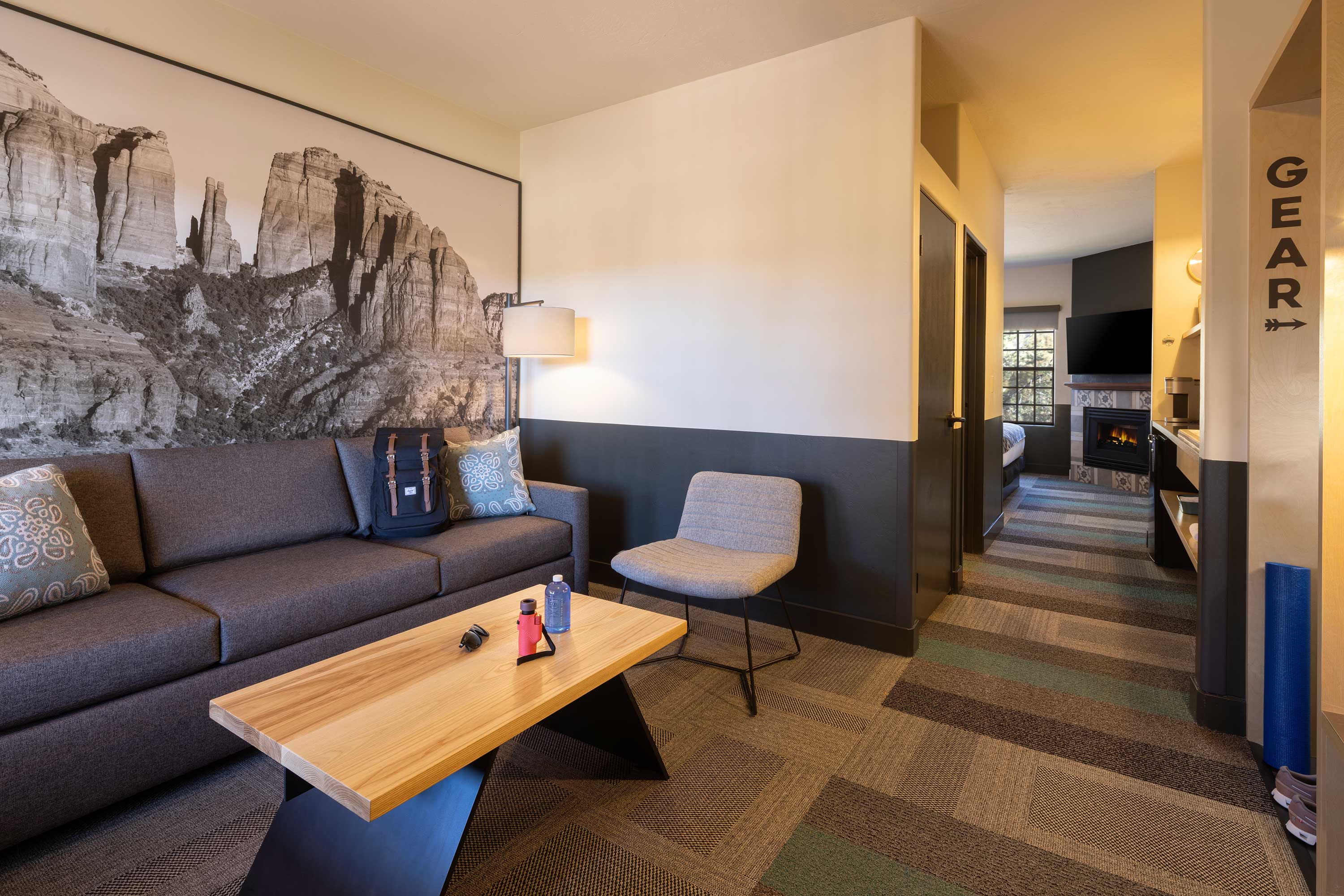 Modern hotel suite living area with a gray sofa, a chair, a wooden coffee table, and a large black-and-white desert rock landscape photo on the wall. Mountain Modern Motel Sedona, immersive hospitality design