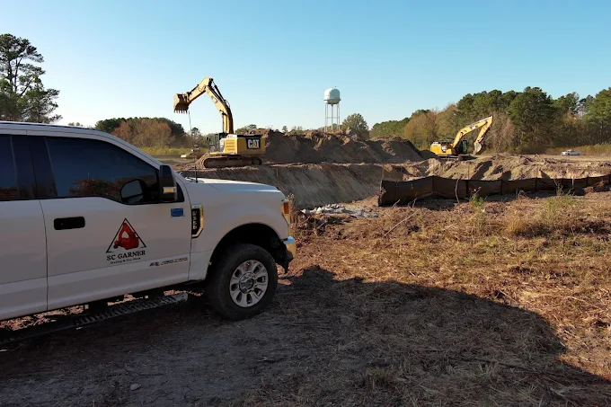 White construction truck at excavation site with heavy machinery and cleared land.
