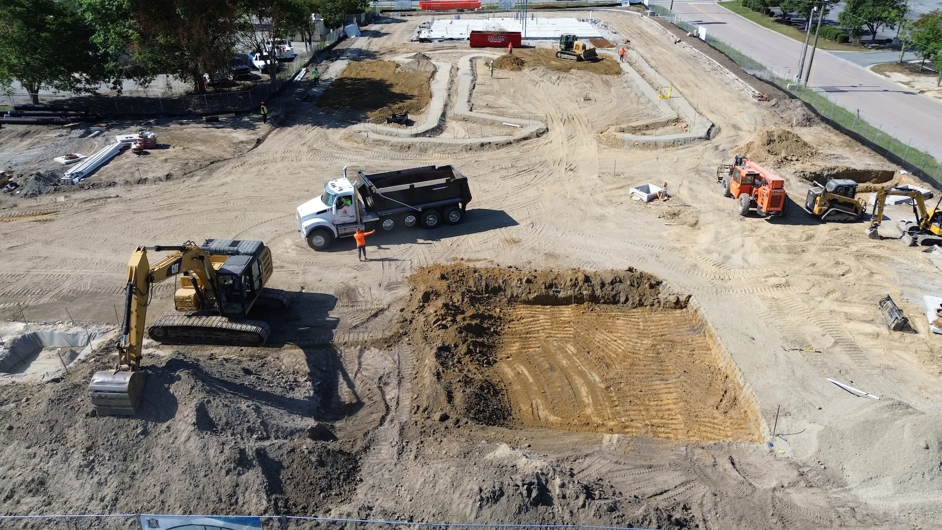 Aerial view of active construction site with heavy machinery, dump truck, and excavated ground.