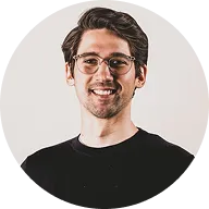 Smiling young man wearing glasses and a black shirt against a light background.
