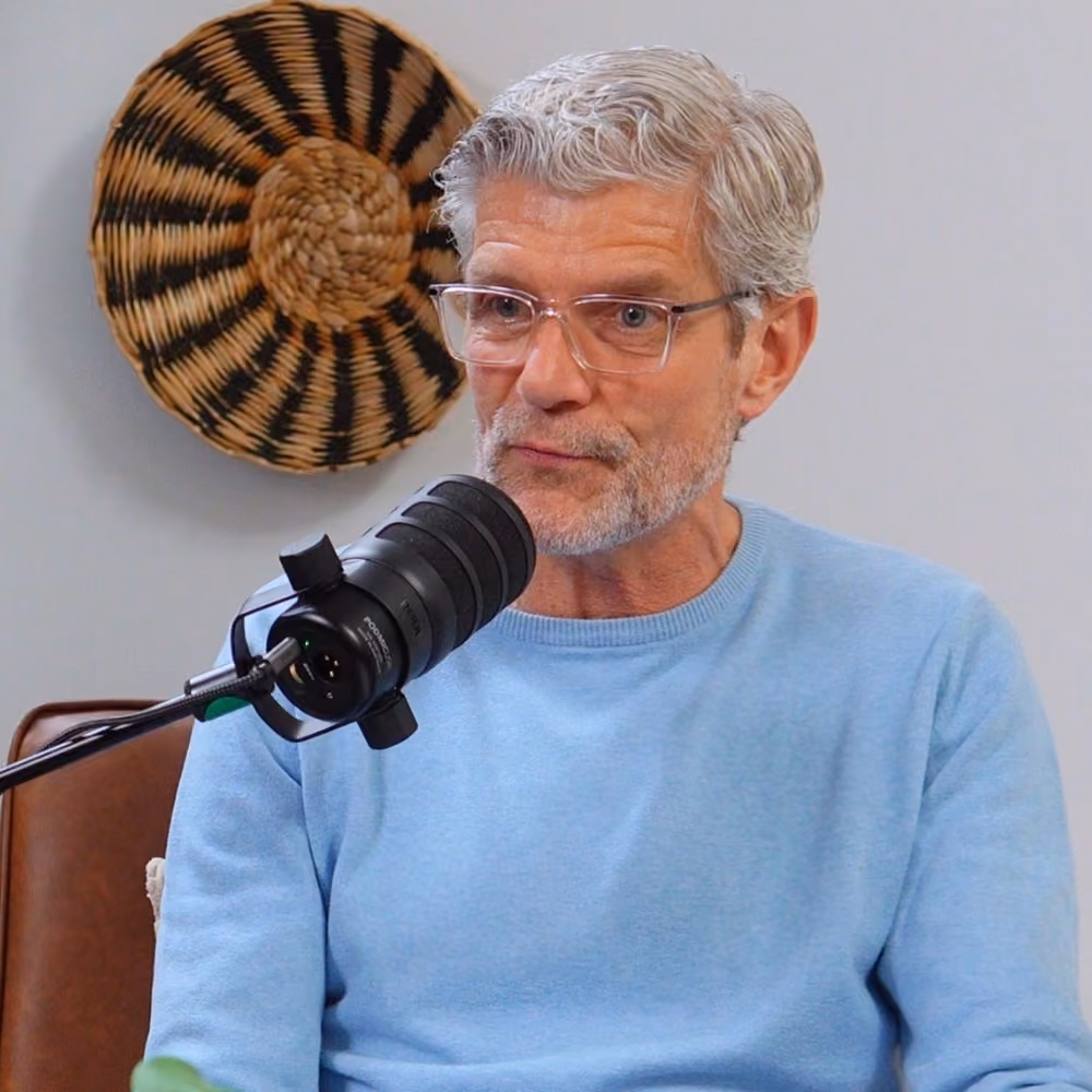 Mann mit Haaren und Brille spricht in ein Mikrofon in einem Podcaststudio.