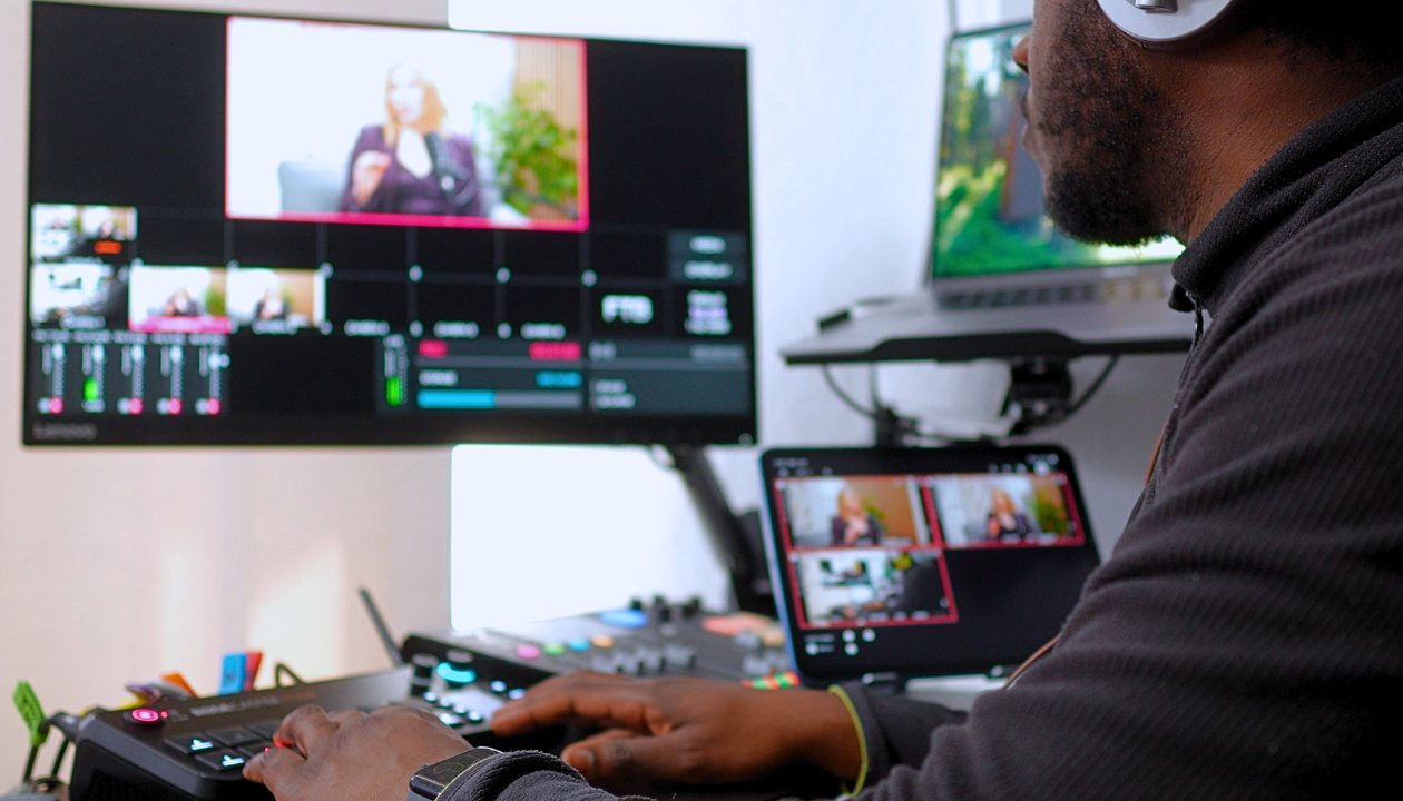 Mann mit Kopfhörern bedient Videomischpult mit Überwachung von Live-Stream-Feeds.