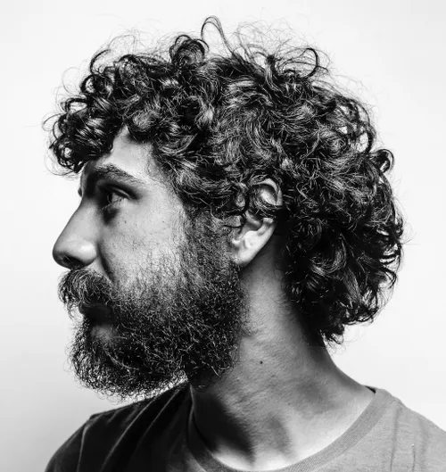 Person with curly hair and a beard in a black and white portrait.