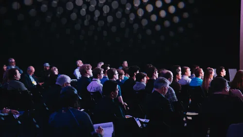 Audience members seated in a dark room, attentively watching a presentation.