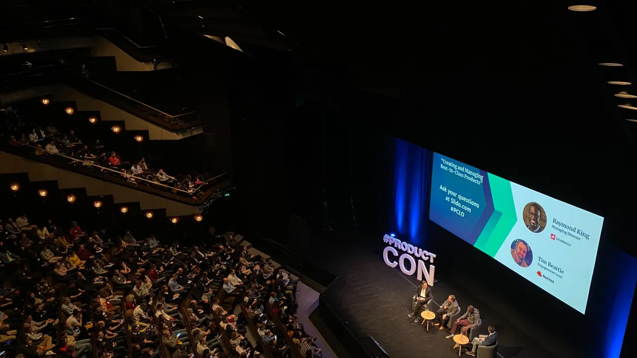 A packed auditorium with attendees watching a panel discussion on stage at a product conference.
