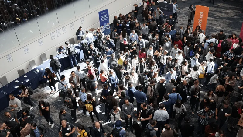 A crowded conference venue with attendees mingling and visiting exhibition tables.