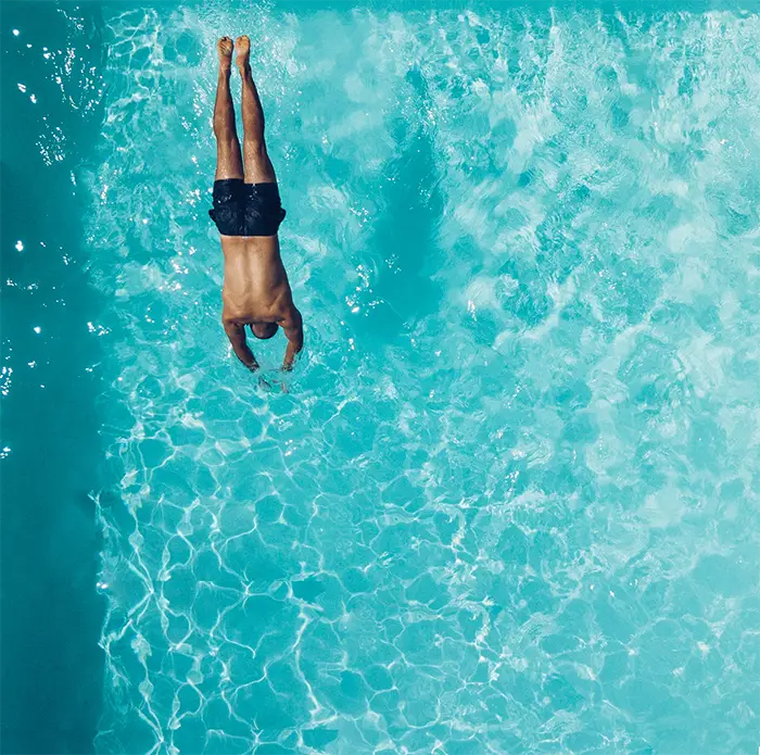 A man in black shorts diving headfirst into a clear blue swimming pool from above.