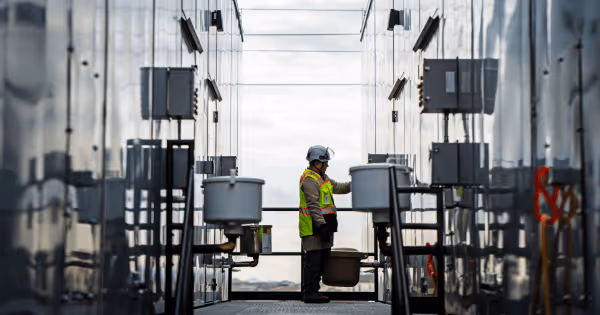 A data center technician in high-visibility gear working between rows of cooling equipment