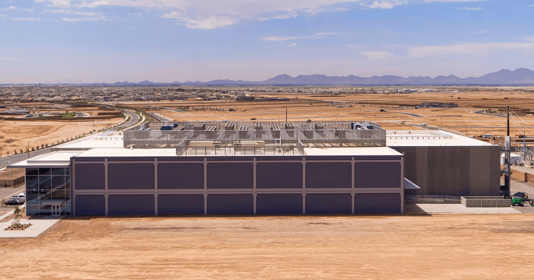 Aerial view of a data center building in a desert setting with mountains in the background