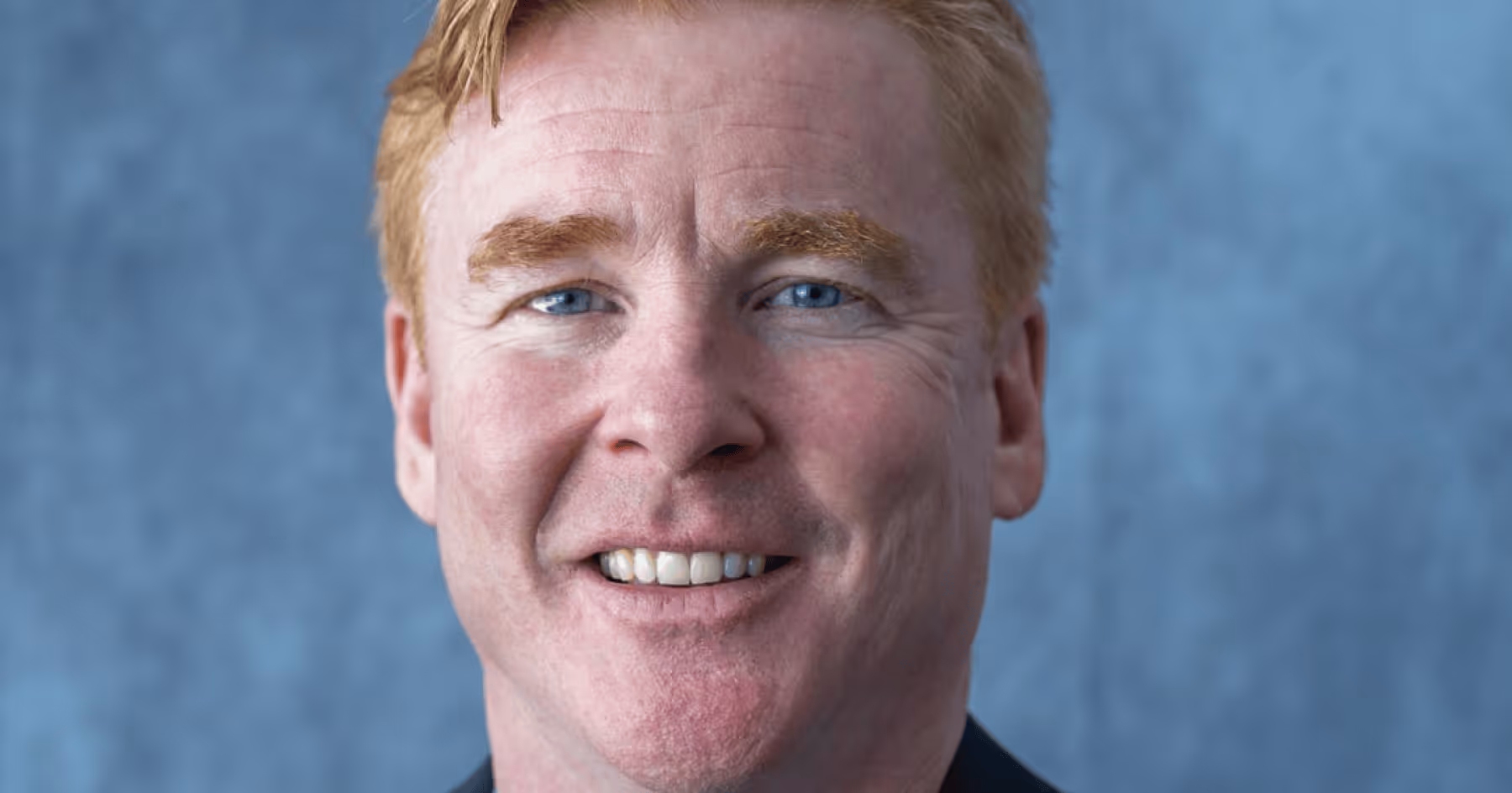 Headshot of John Bean smiling against a blue background