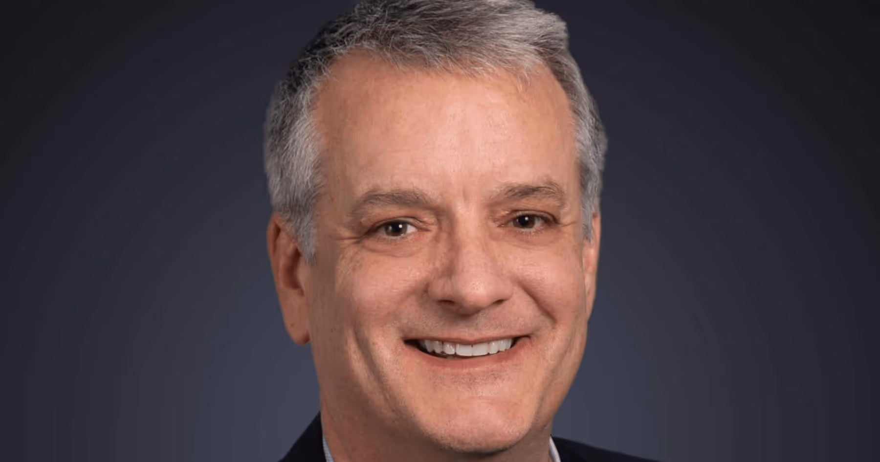 Headshot of Clint Heiden in a suit against a dark background