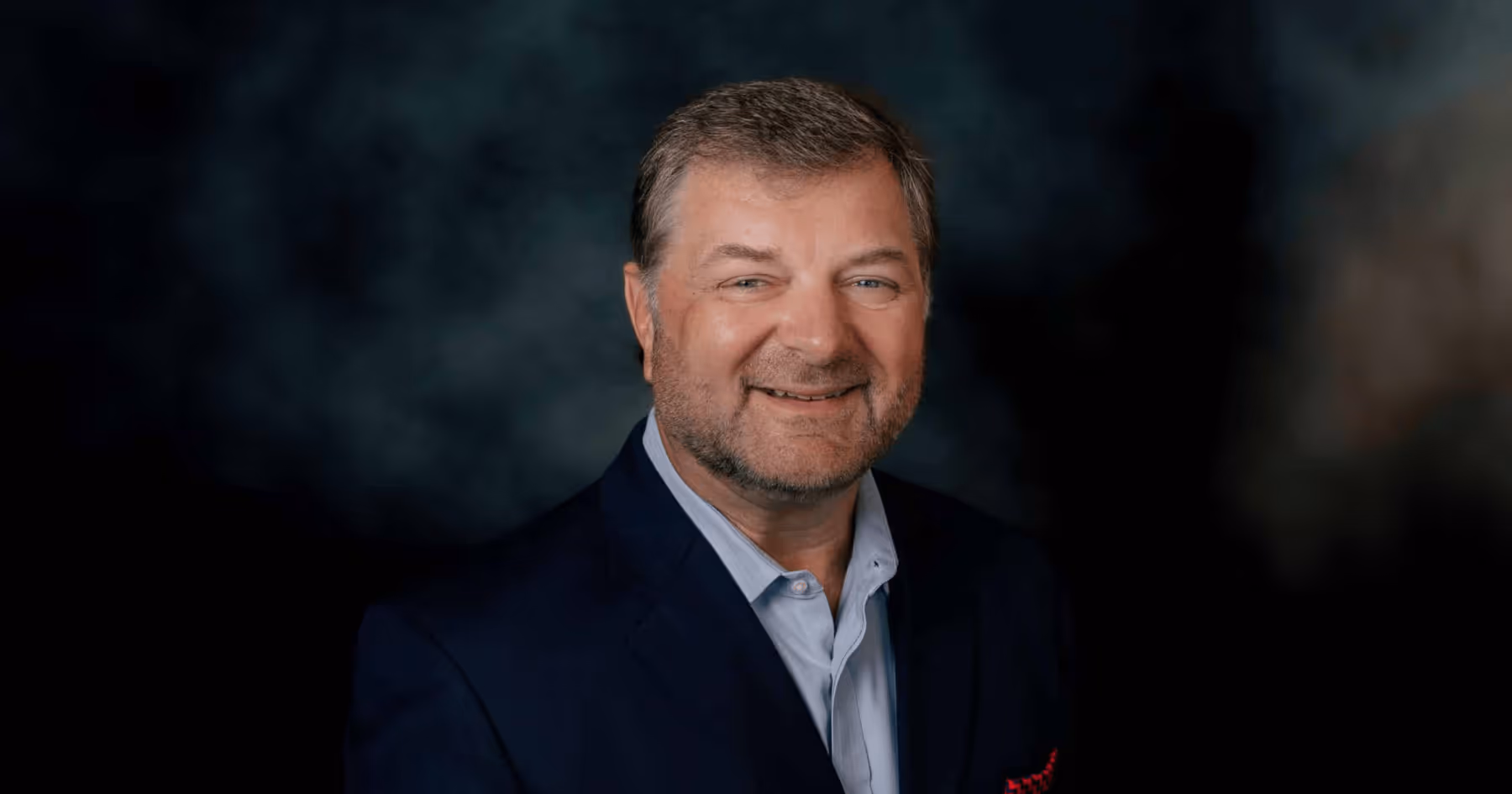Headshot of Bill Jabjiniak in a suit against a dark background