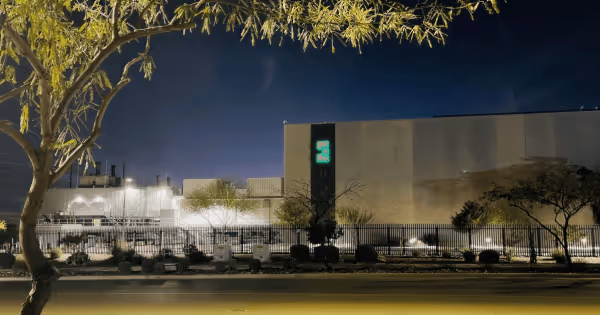 Illuminated data center building exterior at night with a glowing green logo