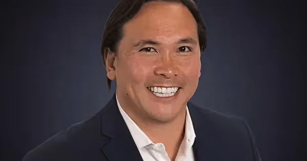 Headshot of Tom Traugott in a suit against a dark background