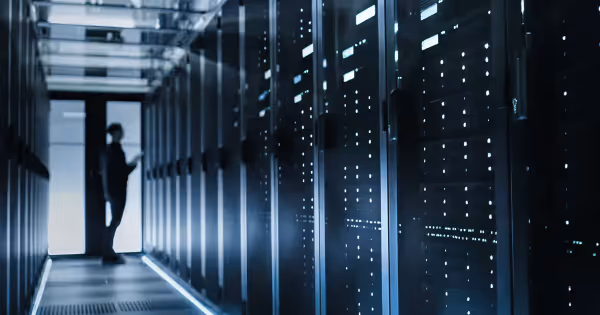 Illuminated server racks in a dark data center corridor with a person standing in the aisle
