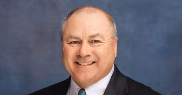 Headshot of a man in a suit smiling against a blue background