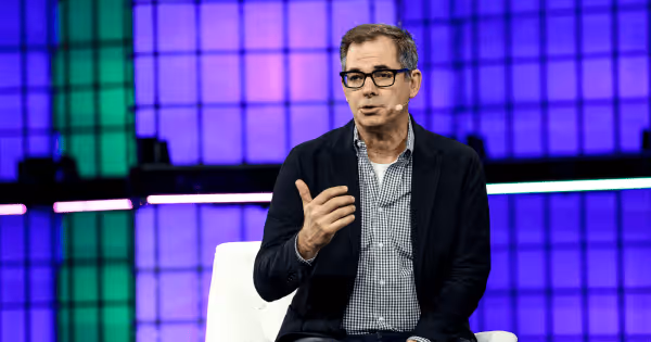 Man speaking on stage at a technology conference in front of a purple LED backdrop