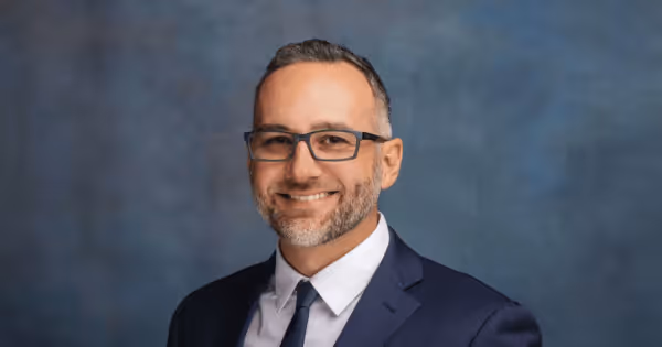 Headshot of a man in a suit against a blue background