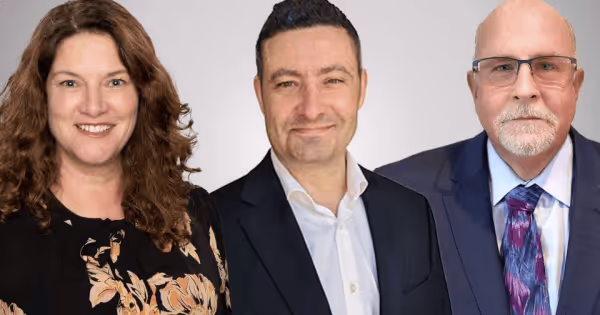 Three professionals smiling together in business attire against a light grey background