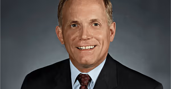Headshot of a man in a suit and tie smiling against a grey background