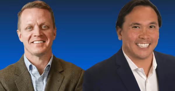 Two men in business casual clothing smiling side by side against a blue background