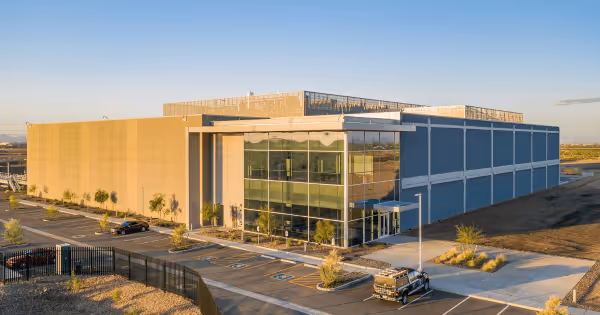Aerial view of a modern data center campus building with a parking lot under a blue sky