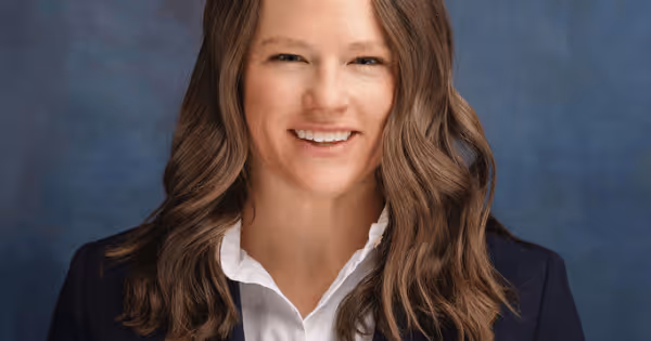 Woman with long brown hair in a dark jacket posing against a dark background