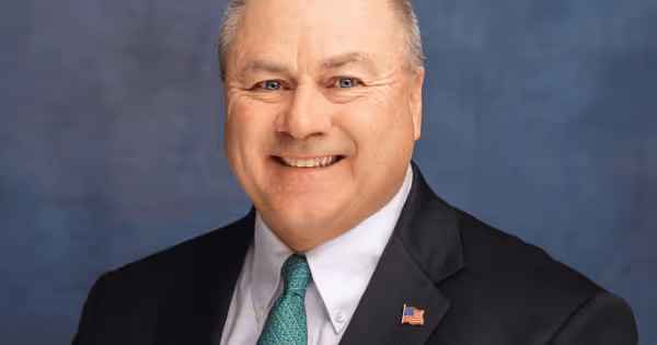 Headshot of a man in a suit smiling against a dark grey background