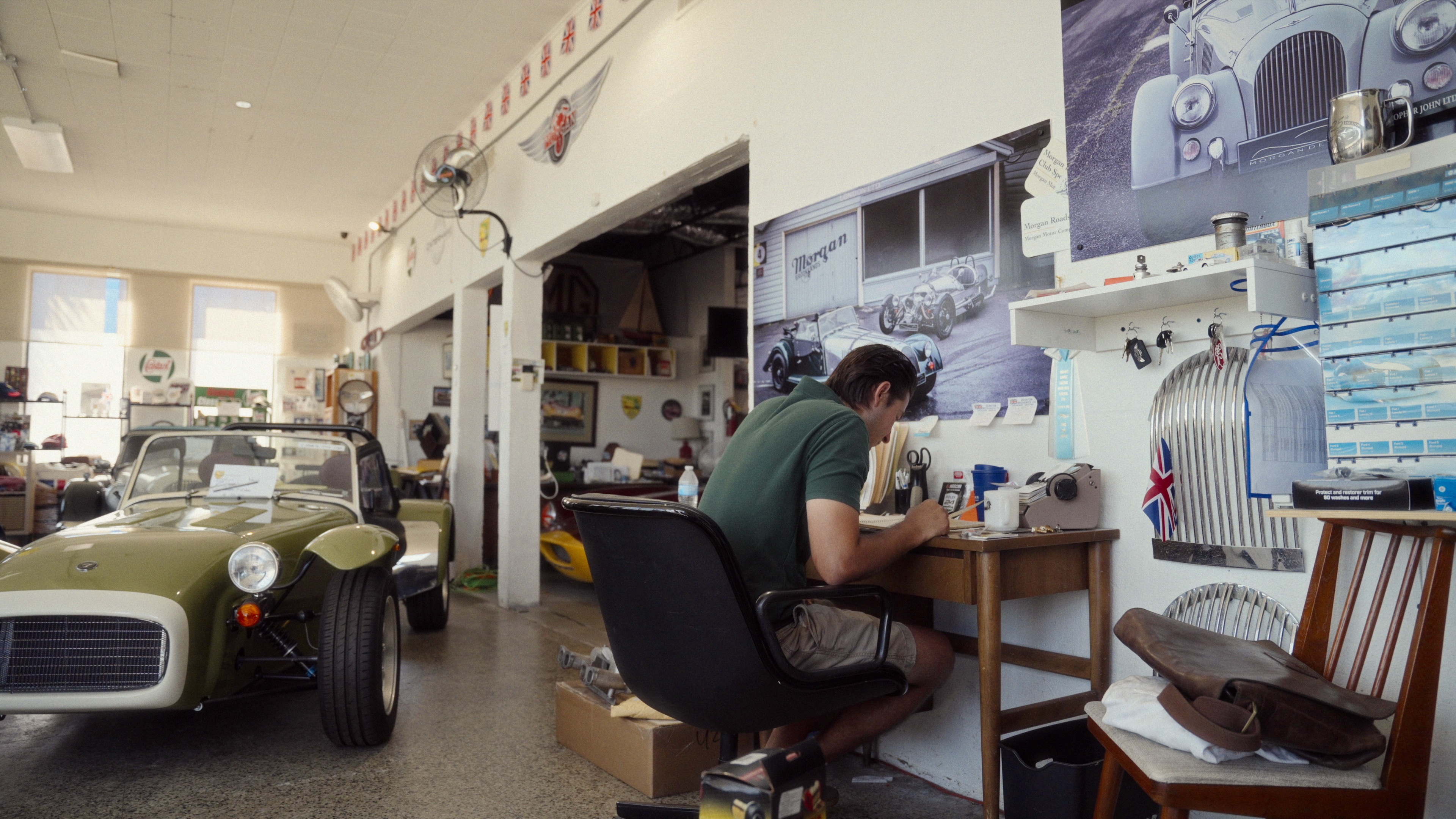 A frame from Engle Digital’s Christopher John, LTD video showing a man working at a desk beside a British sports car