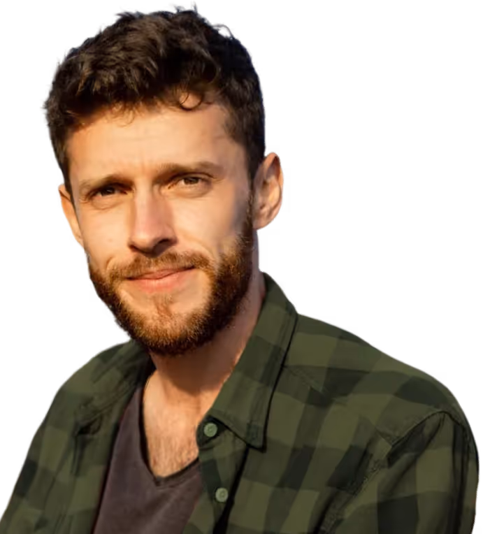 Young man with short curly hair and beard wearing a green plaid shirt over a dark t-shirt, smiling slightly.