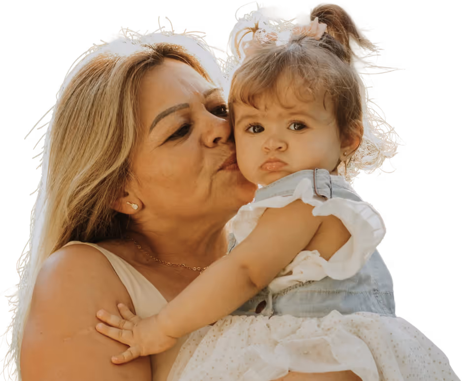 Woman with blonde hair kissing a young girl with a ponytail wearing a denim dress and white skirt.