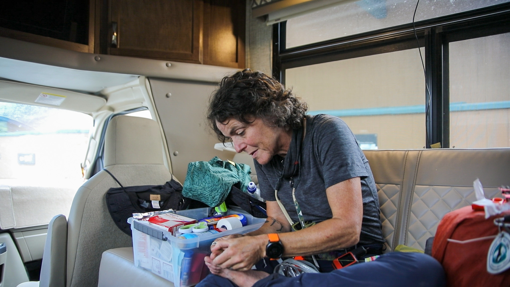 Middle-aged woman sitting inside a vehicle caring for her foot with a first aid kit nearby.
