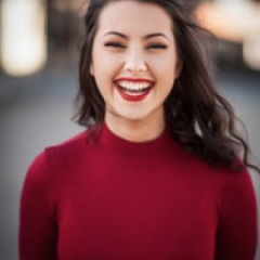 Smiling woman with dark hair wearing a red top against a blurred background.