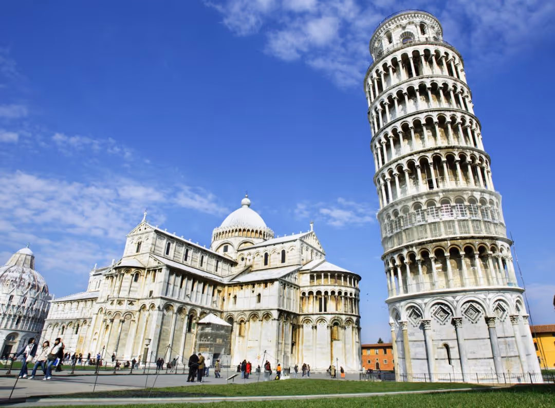 Leaning Tower of Pisa beside Pisa Cathedral under a bright blue sky with scattered clouds.