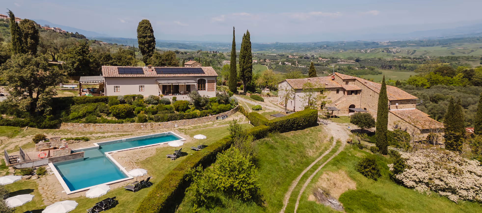 Countryside villa with pool, lounge chairs, tall trees, and rolling hills in the background.