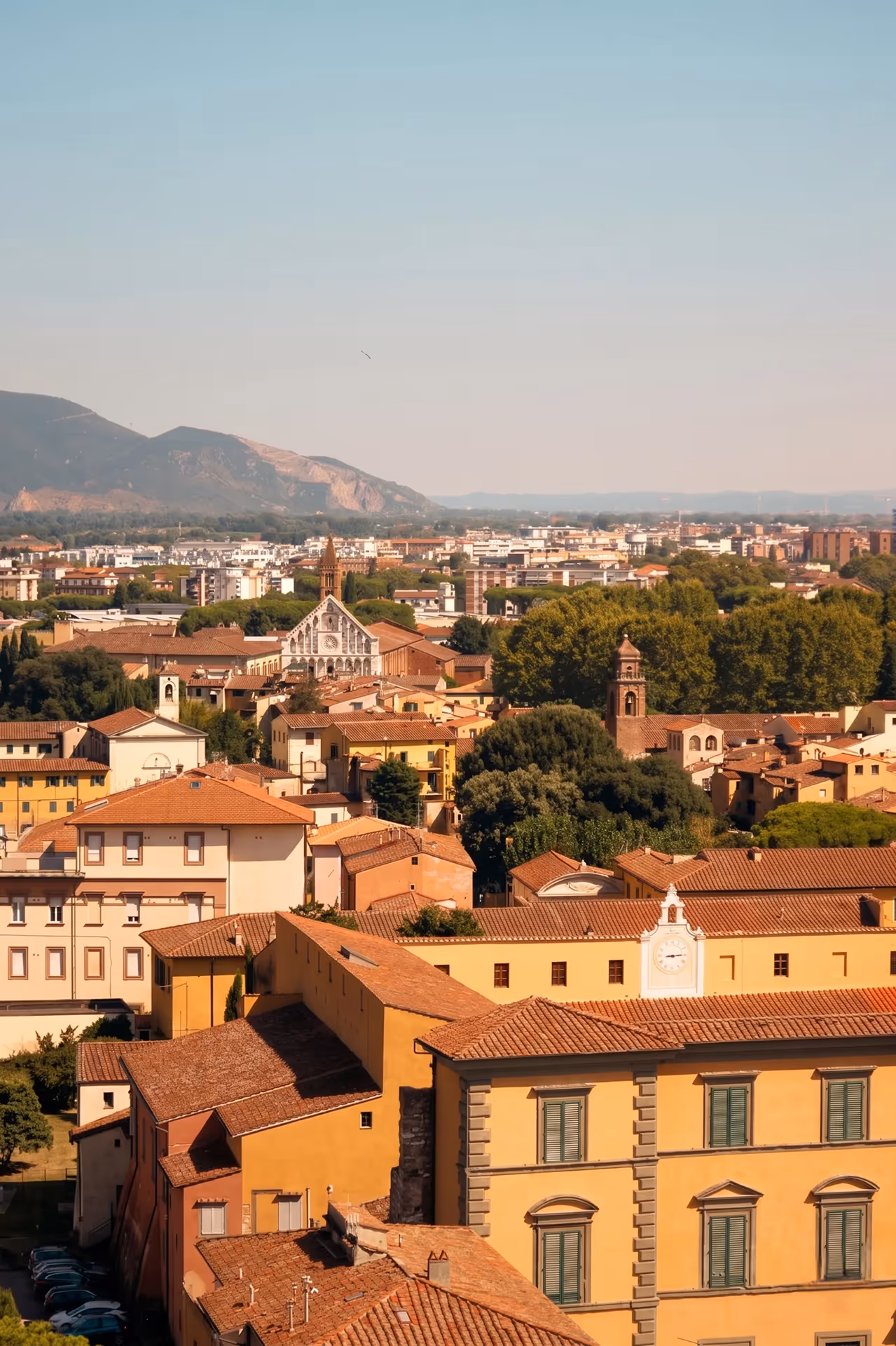 View of a town with terracotta roofs, historic buildings, and mountainous landscape background.
