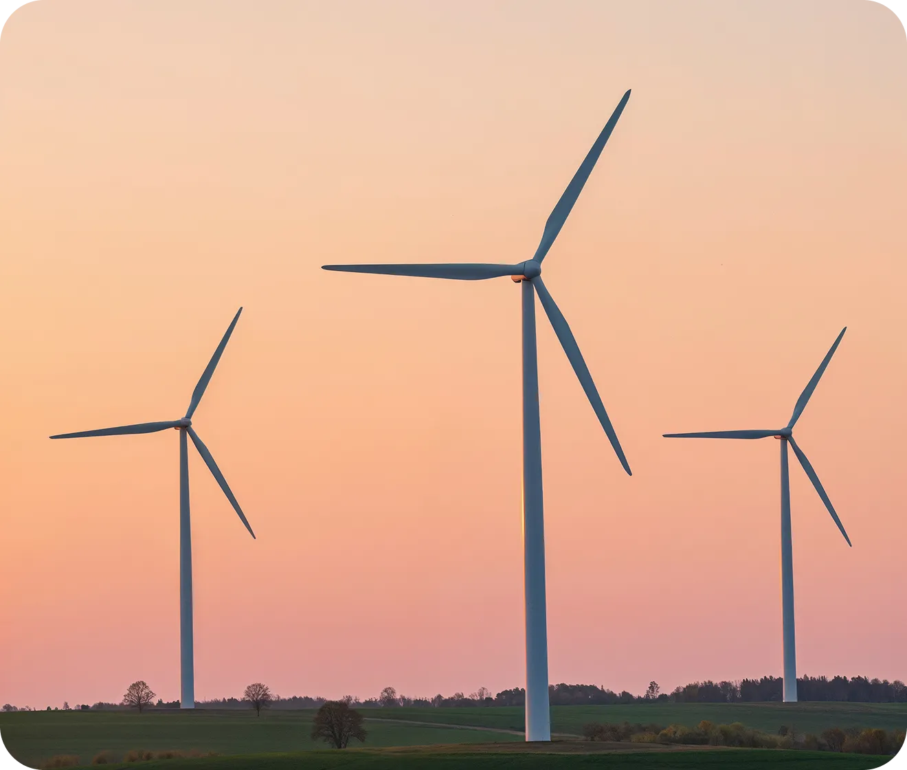 Three large wind turbines standing on green fields under a pink and orange sunset sky.