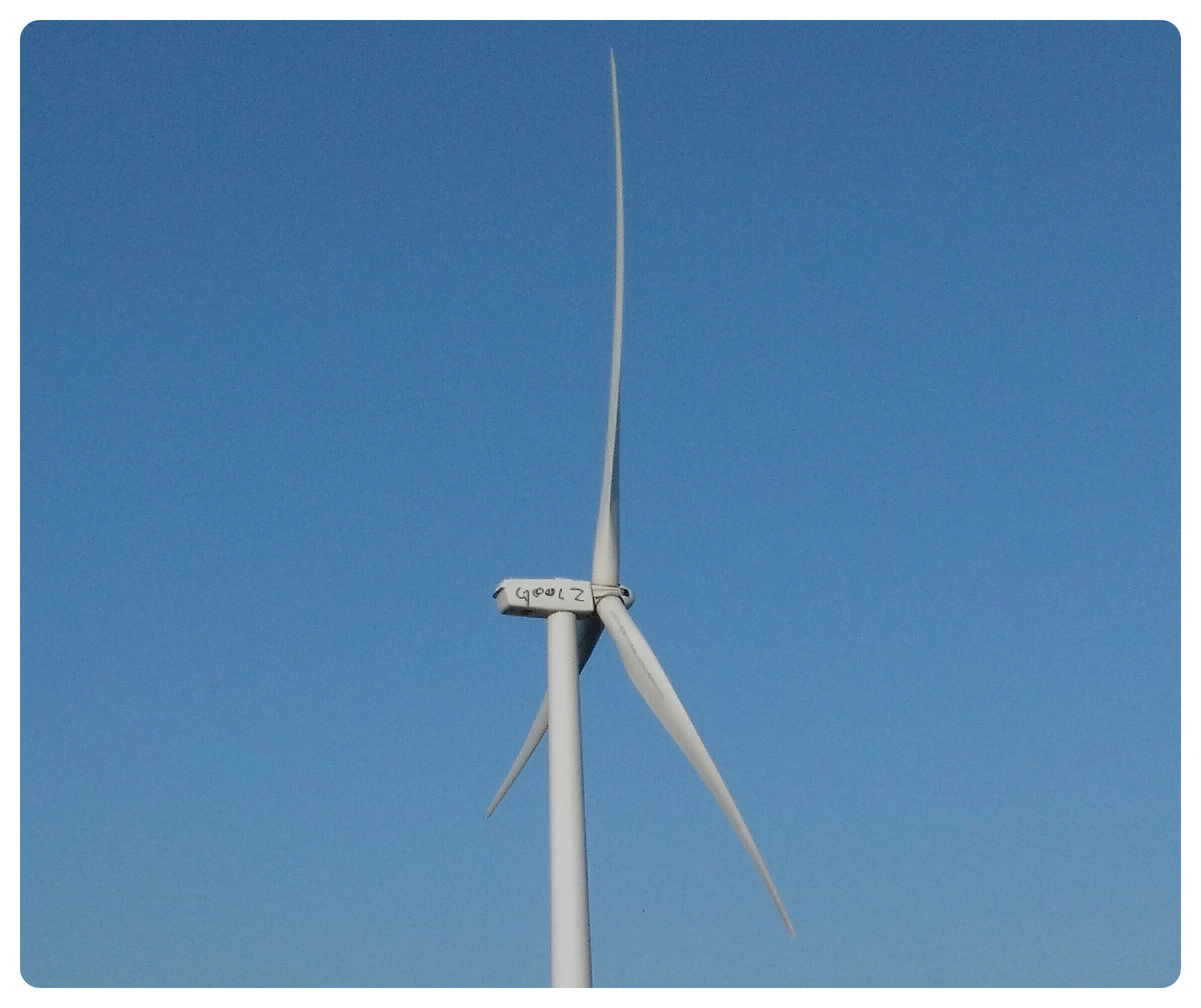 Close-up of a white wind turbine with three blades against a clear blue sky.