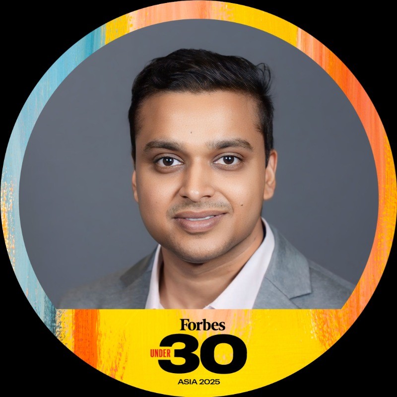 Woman with long dark hair smiling outdoors, wearing large gold earrings.